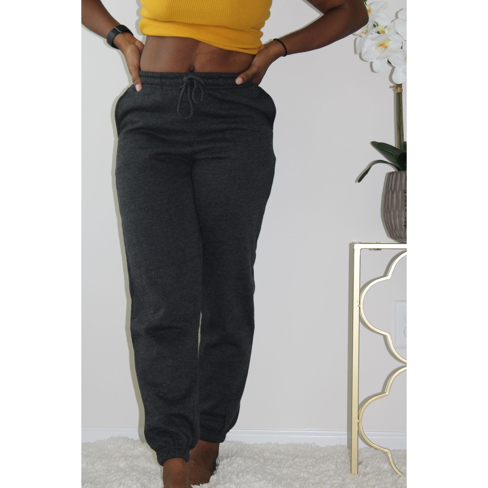 Charcoal sweatpants with side pockets, 2-inch elastic waistband, and elastic cuffs at the ankles, made from 60% cotton and 40% polyester for a comfortable, casual look. Model is 5'4" wearing a small. Model facing front with her hands on the waist of the sweatpants