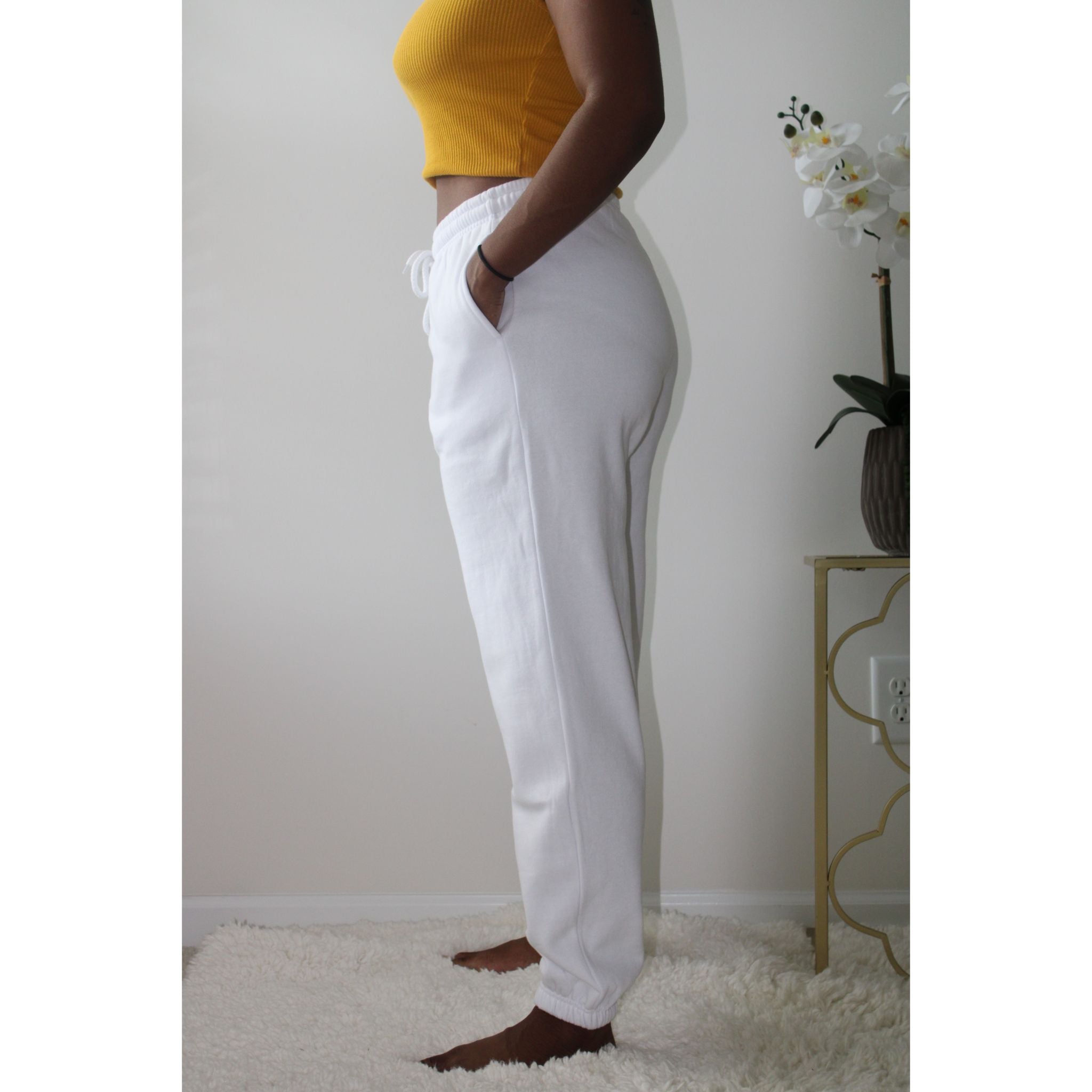 White sweatpants with side pockets, made from 60% cotton and 40% polyester, featuring a 2-inch elastic waistband and elastic cuffs at the ankles for a comfortable, casual style. Model is 5'4" wearing a small. Side view left