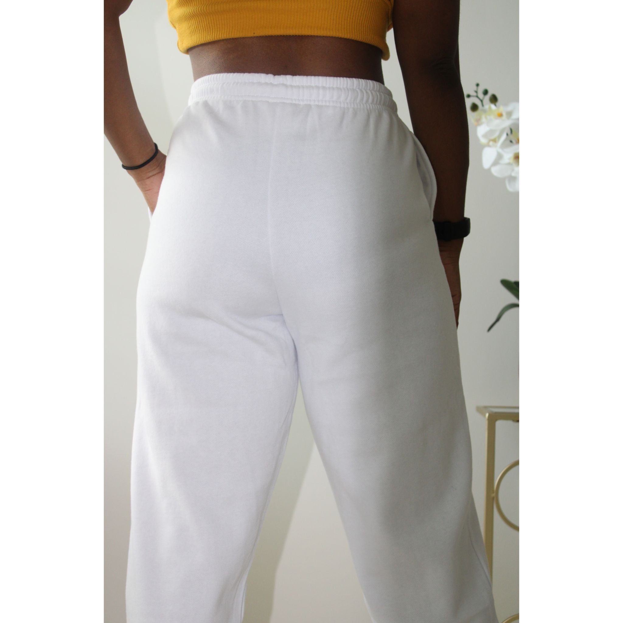 White sweatpants with side pockets, made from 60% cotton and 40% polyester, featuring a 2-inch elastic waistband and elastic cuffs at the ankles for a comfortable, casual style. Model is 5'4" wearing a small. Close up back view