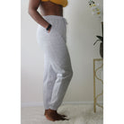 Heather grey sweatpants with side pockets, 2-inch elastic waistband, and elastic cuffs at the ankles, made from 60% cotton and 40% polyester for a comfortable, casual look. Model is 5'4" wearing a small. Side view with hands in pockets