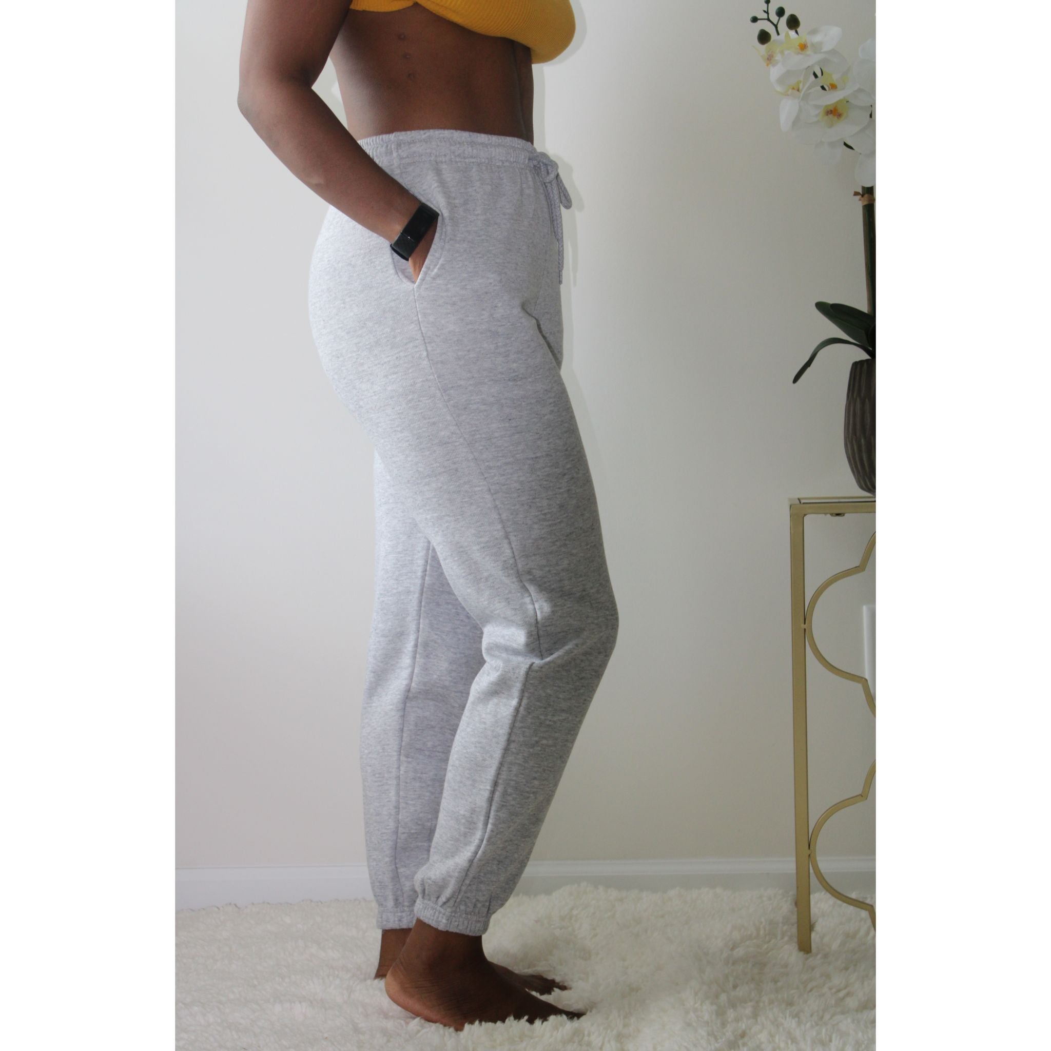 Heather grey sweatpants with side pockets, 2-inch elastic waistband, and elastic cuffs at the ankles, made from 60% cotton and 40% polyester for a comfortable, casual look. Model is 5'4" wearing a small. Side view with hands in pockets