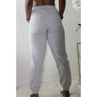 Heather grey sweatpants with side pockets, 2-inch elastic waistband, and elastic cuffs at the ankles, made from 60% cotton and 40% polyester for a comfortable, casual look. Model is 5'4" wearing a small. Back view hands in pockets